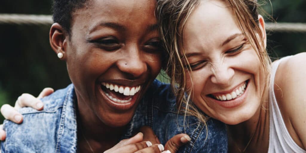Duas mulheres homoafetivas sorrindo e abraçadas, demonstrando carinho e cumplicidade em um momento de felicidade.