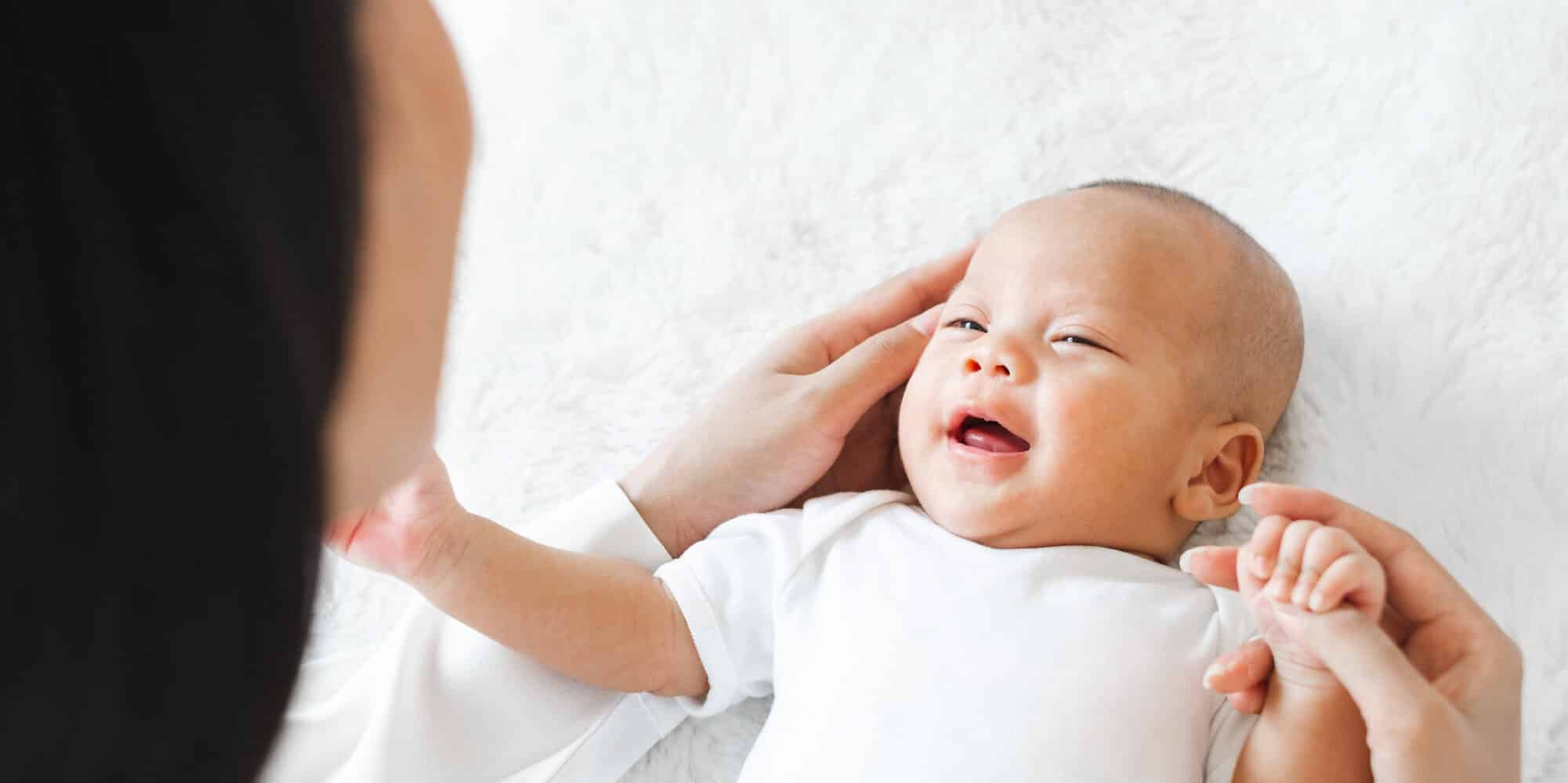 Bebê sorridente deitado, sendo acariciado com carinho por uma pessoa adulta, representando o sonho da maternidade para mulheres trans.