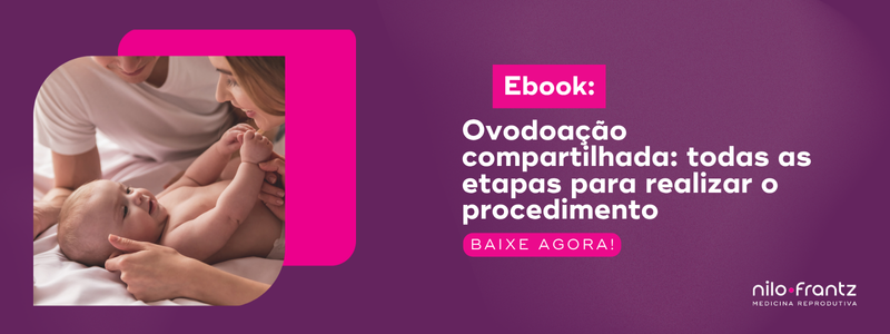Casal sorrindo e olhando para um bebê deitado na cama, ao lado de banner sobre ovodoação compartilhada.