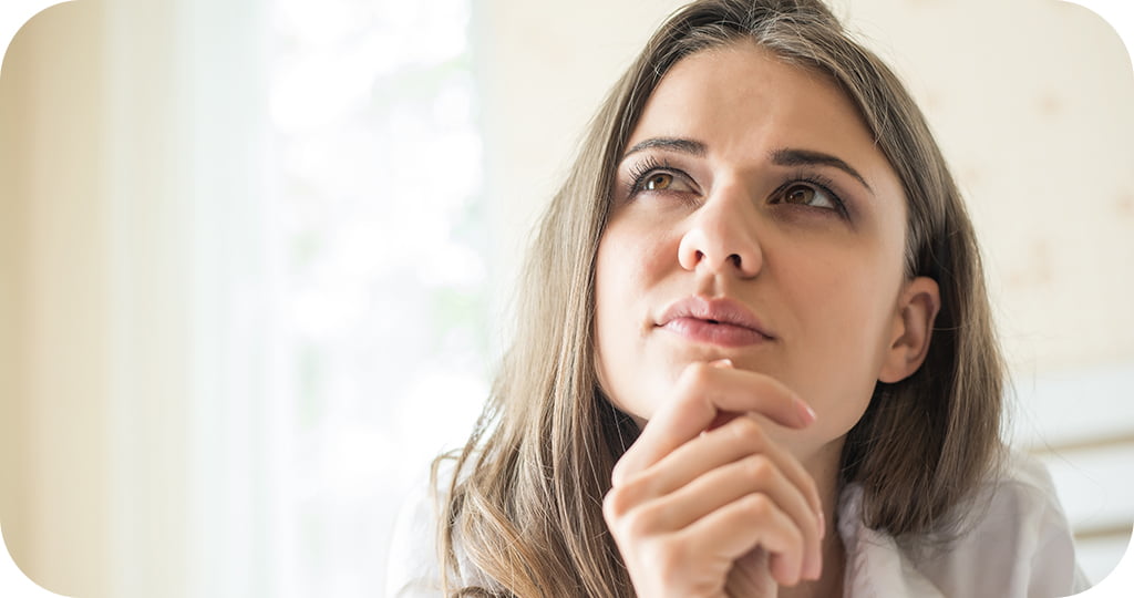 Uma mulher jovem com cabelos castanhos, lisos e compridos, em uma pose pensativa.