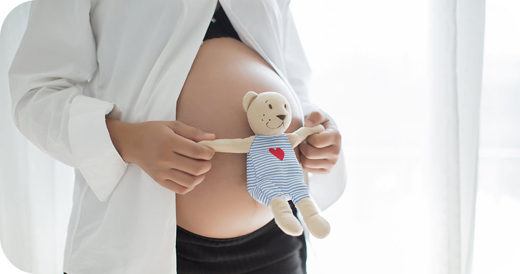 Mulher grávida segurando ursinho de pelúcia sobre a barriga, simbolizando o afeto e o cuidado envolvidos na barriga solidária no Brasil.