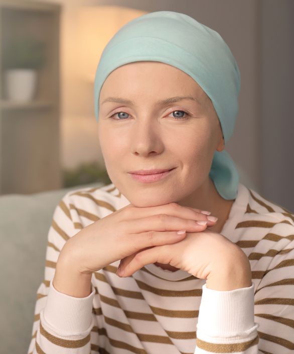 Mulher com lenço na cabeça, sorrindo levemente, com as mãos apoiadas no queixo. Ela transmite serenidade e força. Imagem associada à Nilo Frantz Medicina Reprodutiva.