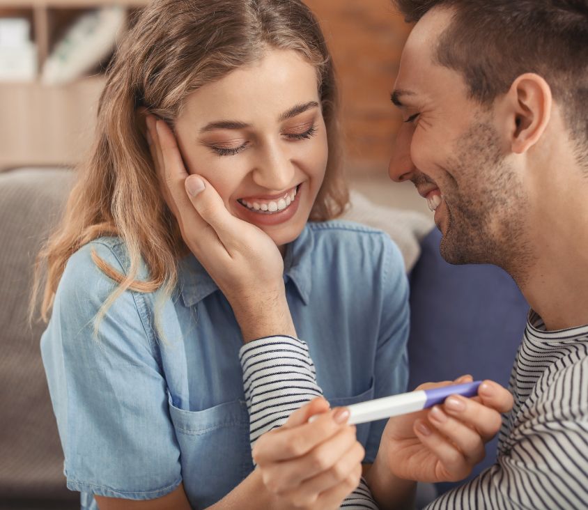Casal sorridente comemora resultado positivo de teste de gravidez, representando a emoção de alcançar o sonho da maternidade e paternidade.