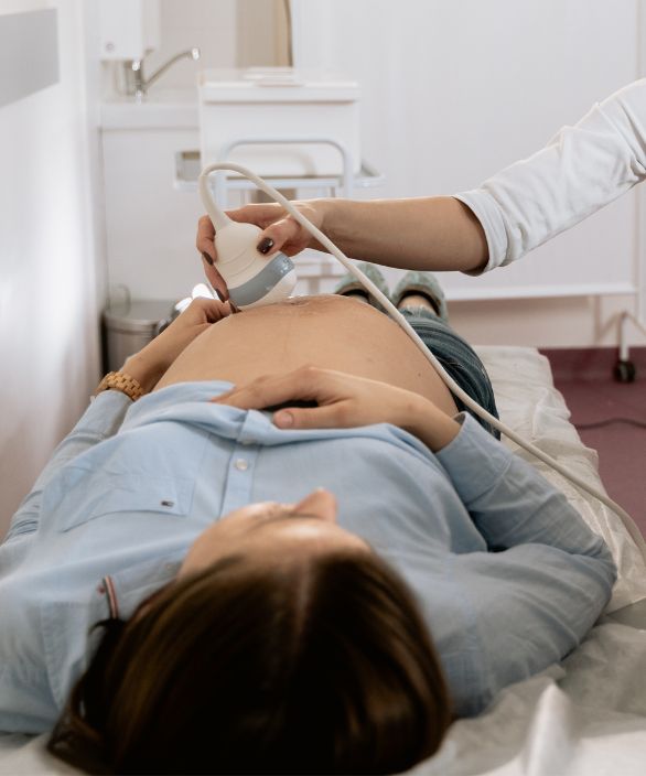 Mulher grávida deitada em uma maca durante exame de ultrassom, realizado por profissional da saúde. Imagem relacionada à Nilo Frantz Medicina Reprodutiva.