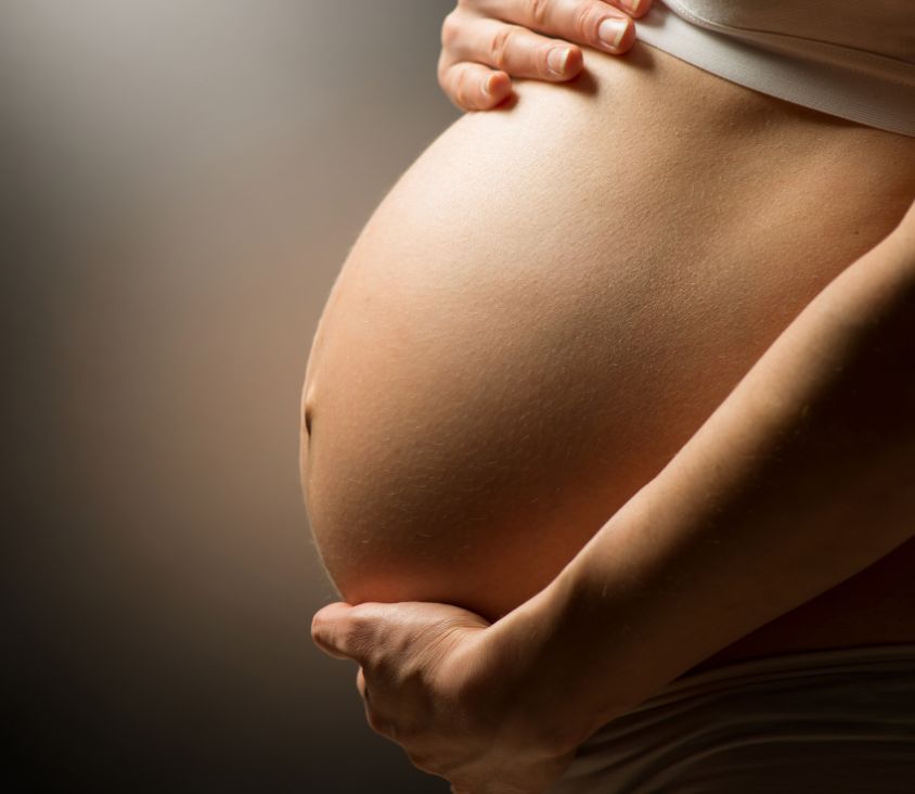 Mulher grávida segurando a barriga com ambas as mãos, transmitindo carinho e proteção ao bebê que está por vir.