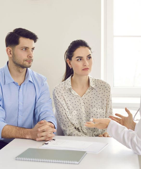 Casal atento em consulta médica com especialista em reprodução assistida, sentados à mesa com documentos e cadernos à frente.