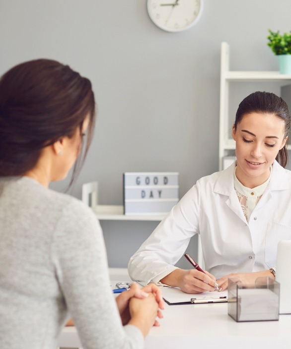 Médica atendendo uma paciente em consultório, ambas sentadas frente a frente, demonstrando acolhimento e atenção durante a consulta