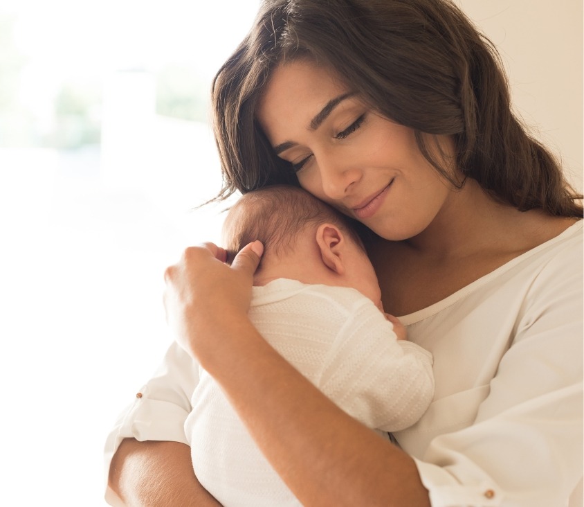 Mulher segurando seu bebê recém-nascido com carinho, em um momento de afeto e tranquilidade, com expressão de plenitude e amor.