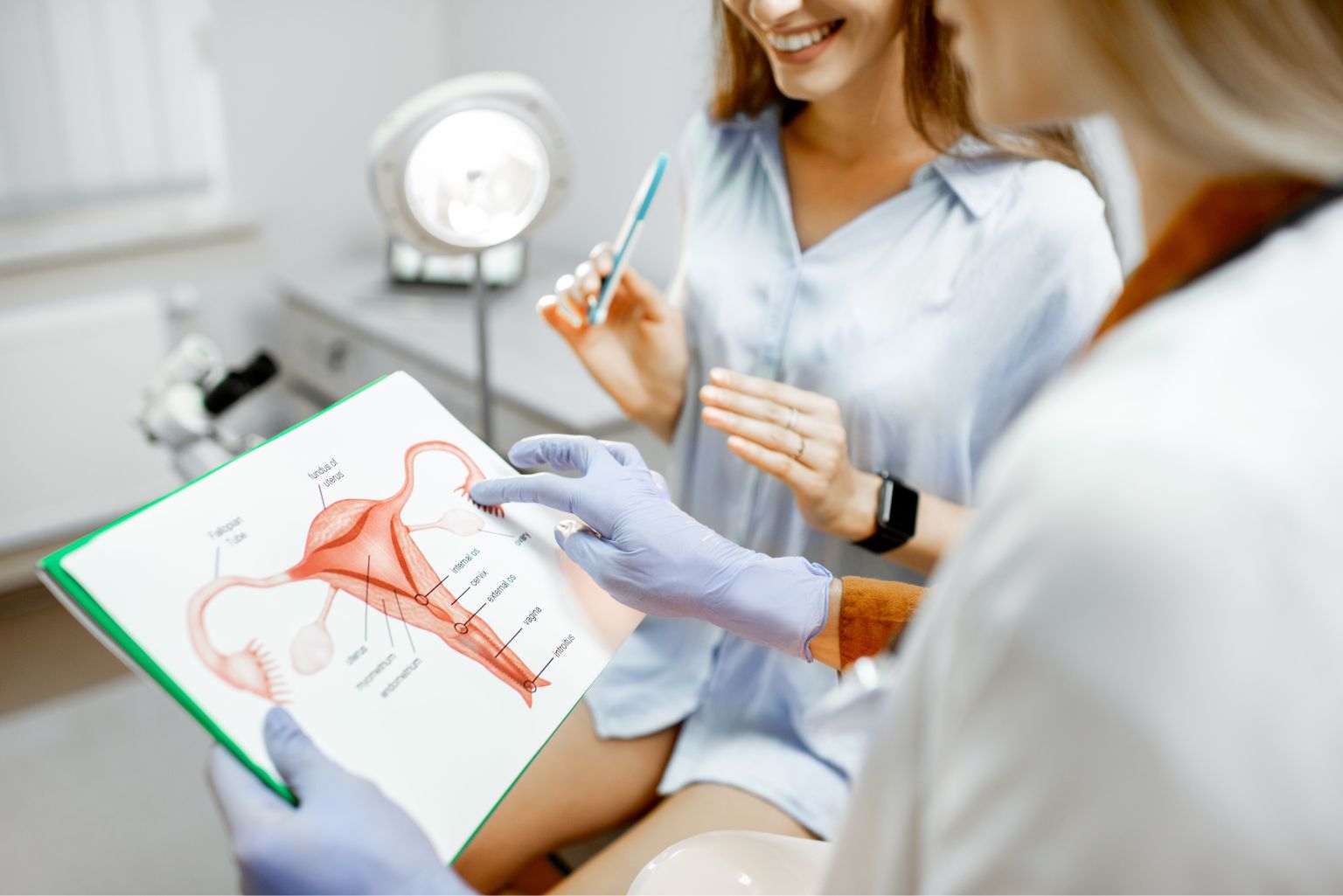 Profissional da saúde explica o sistema reprodutor feminino utilizando uma ilustração anatômica, em consulta médica com paciente sorridente. O cenário é de um consultório ginecológico, simbolizando acolhimento e orientação especializada sobre fertilidade.