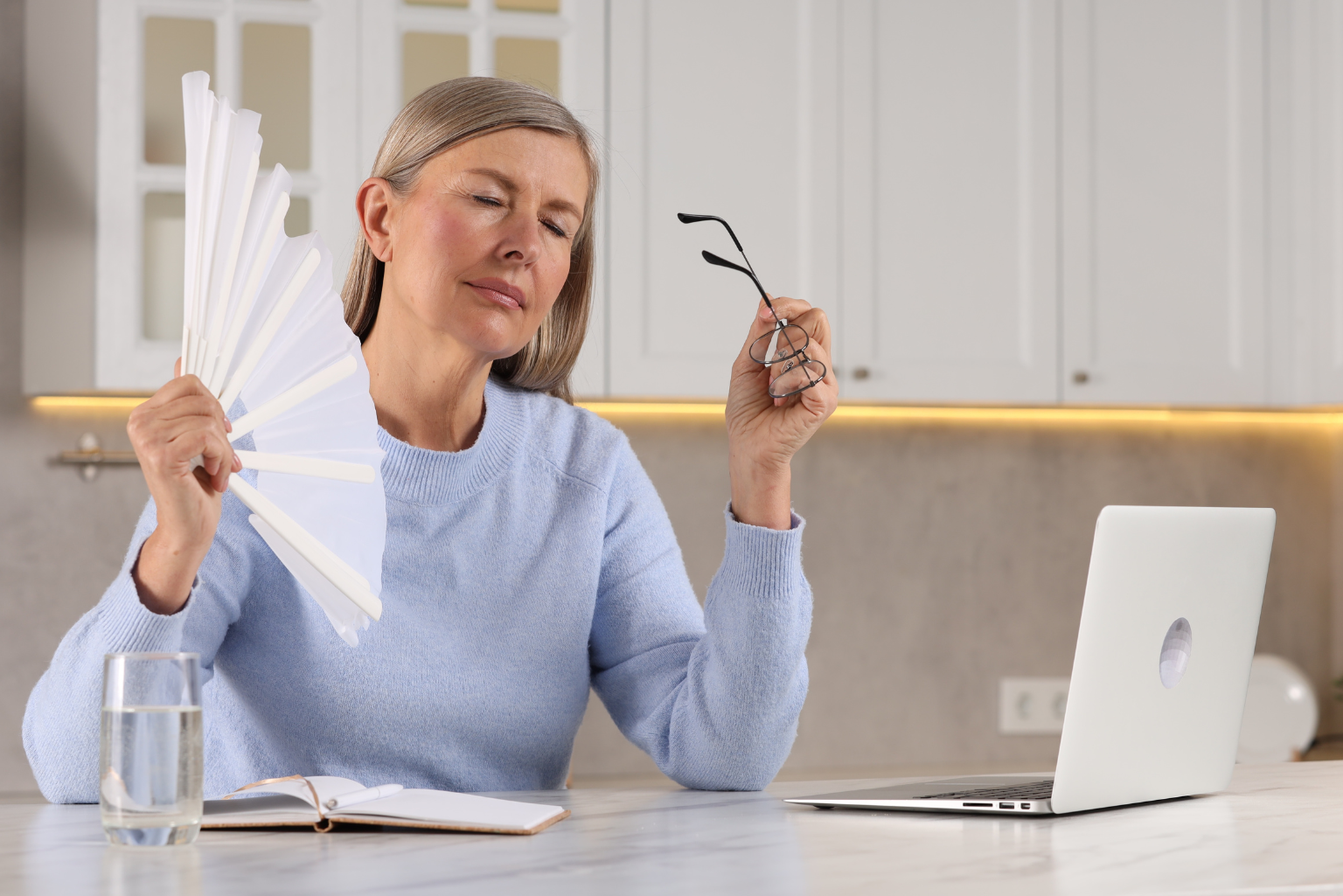 Mulher de meia-idade com ventilador de papel, sentindo calor intenso durante o climatério