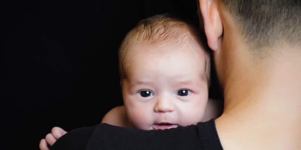 Bebê no colo de um homem trans, simbolizando paternidade e gestação transmasculina.