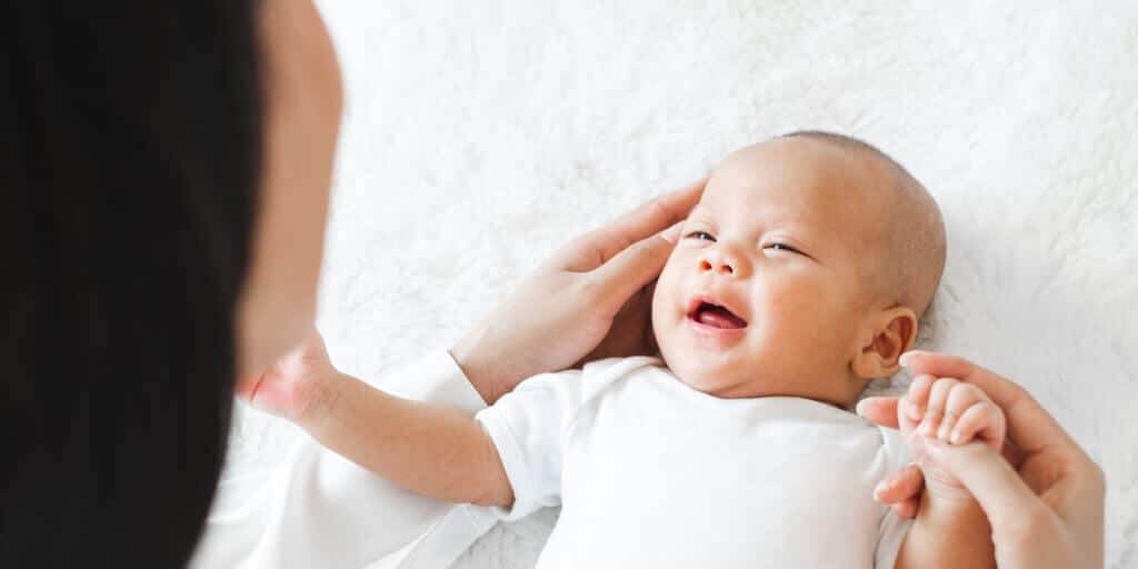 Bebê sorridente deitado, sendo acariciado com carinho por uma pessoa adulta, representando o sonho da maternidade para mulheres trans.