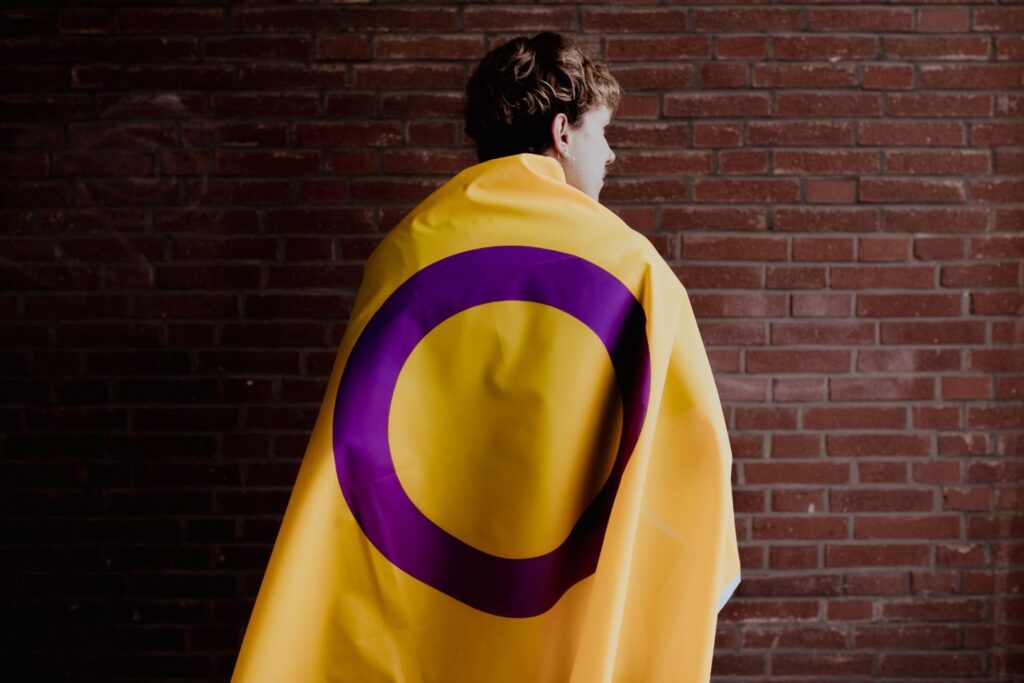 Pessoa de costas com bandeira intersexo sobre os ombros, simbolizando intersexo e reprodução assistida.
